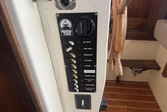 Slide: The Image of Control panel of a 1983 Nordic Tug 26 boat with switches and wooden steering wheel. - 21