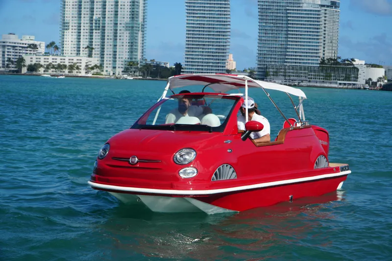 Slide: The Image of Red Fiat 500 Classic boat on water, city skyline in background, 2025 model. - 1