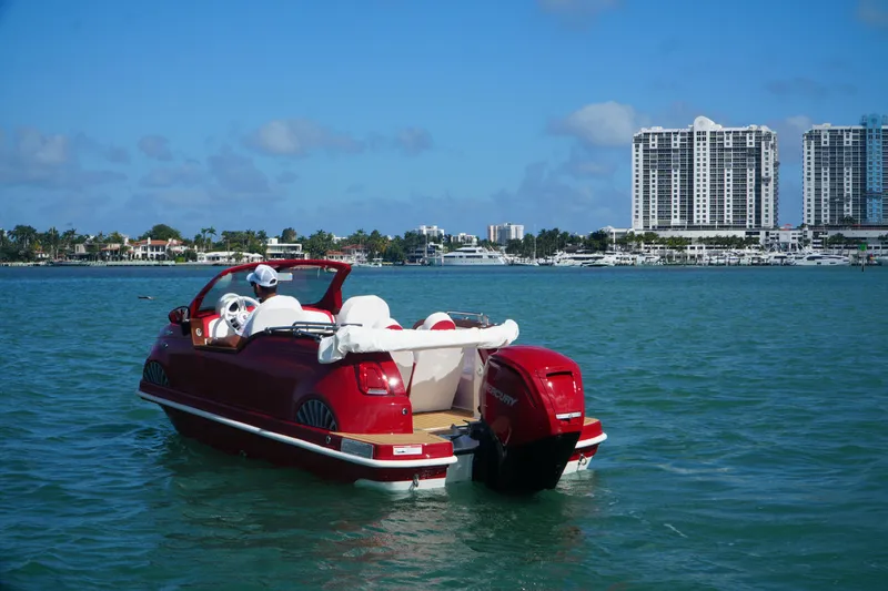 Slide: The Image of Red Car Off-shore Fiat 500 Classic boat on water, city skyline in background, 2025 model. - 16