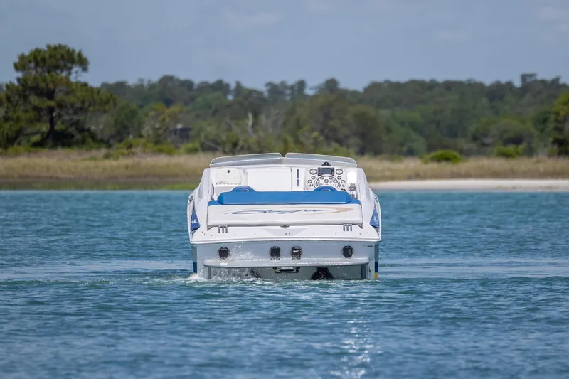 Slide: The Image of 2014 Baja 35 Outlaw boat cruising on a serene lake with forested shoreline. - 7