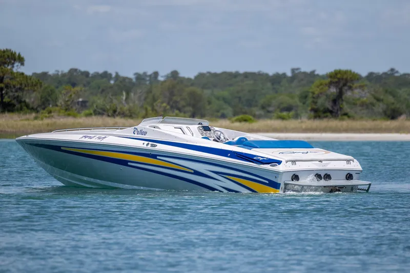 Slide: The Image of 2014 Baja 35 Outlaw speedboat cruising on a serene lake with lush greenery. - 8