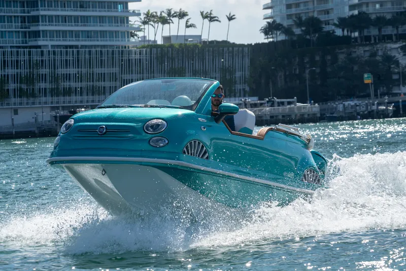 Slide: The Image of 2025 Car Off-shore Fiat 500 Classic boat cruising on water near urban skyline. - 2