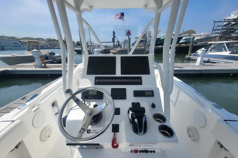 Slide: The Image of Edgewater 245CC 2022 boat dashboard with steering wheel and controls at marina. - 60
