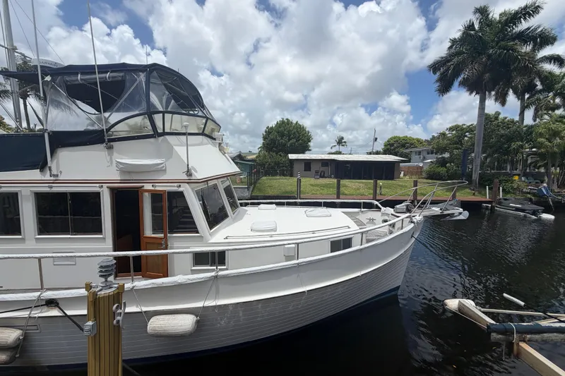 Slide: The Image of 1991 Grand Banks 46 Classic yacht docked by palm trees under a cloudy sky. - 36