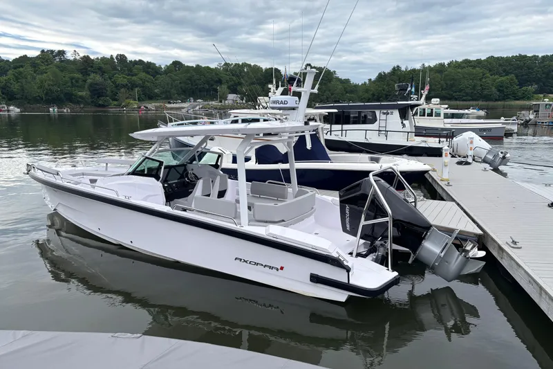 Slide: The Image of 2025 Axopar 29 Sun-Top boat docked on a calm lake with lush greenery. - 2