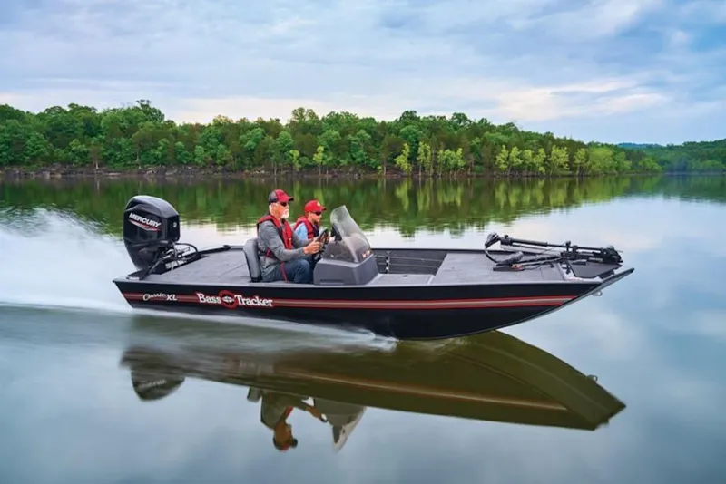The Image of 2026 Tracker Bass Tracker Classic XL boat cruising on a serene lake with lush green trees. - 1