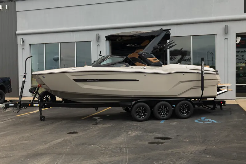 Slide: The Image of 2026 MasterCraft X24 boat on trailer, parked outside a building. - 2