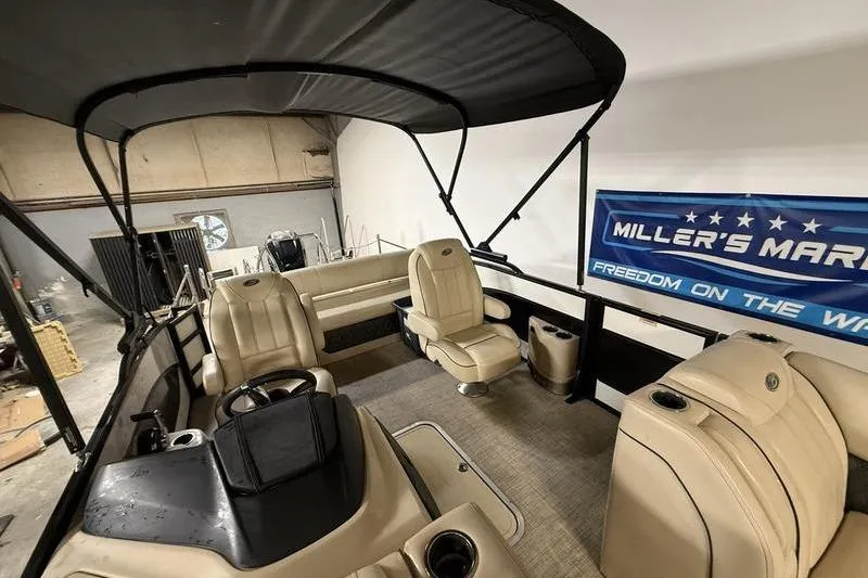 Slide: The Image of 2020 Barletta L23UC pontoon boat interior with beige seating and canopy in showroom. - 12