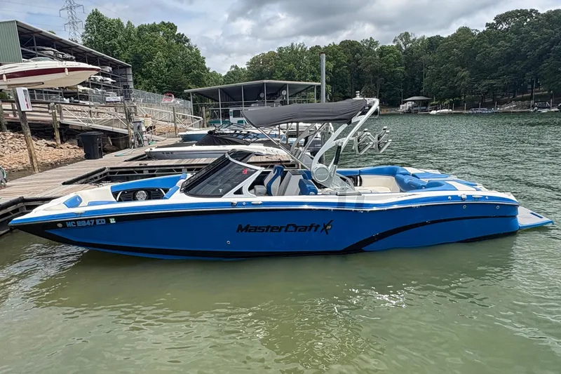 The Image of 2016 MasterCraft X26 boat docked on a lake with lush green surroundings. - 1