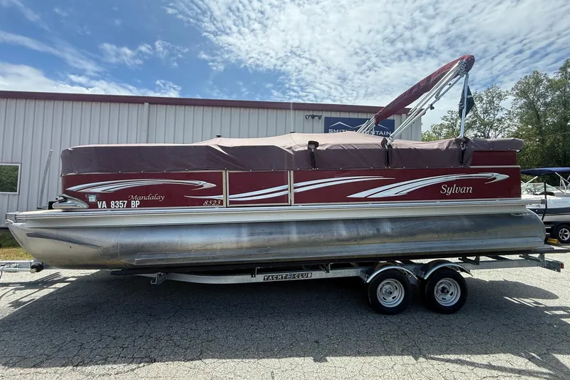 The Image of 2008 Sylvan 8523 Mandalay RE pontoon boat on trailer, parked outside a building. - 1