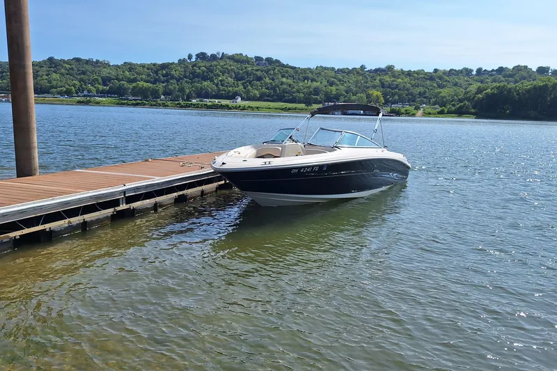 Slide: The Image of 2004 Sea Ray 240 Select boat docked on a serene lake with lush green hills. - 24