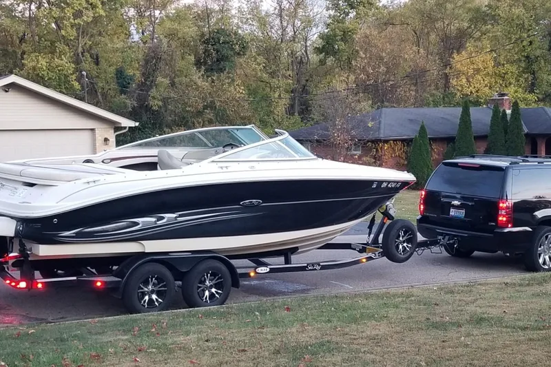 Slide: The Image of 2004 Sea Ray 240 Select boat on trailer, towed by a black SUV in suburban setting. - 26