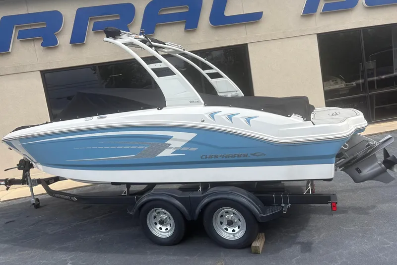 Slide: The Image of 2026 Chaparral 21 SSi boat on trailer, blue and white design, parked outside dealership. - 2