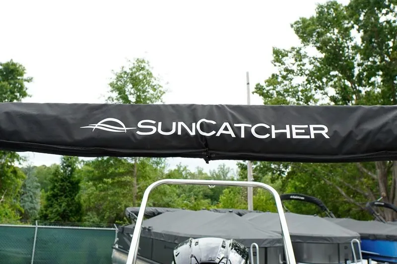 Slide: The Image of 2026 SunCatcher Select 322SL boat canopy with logo, surrounded by lush greenery. - 47