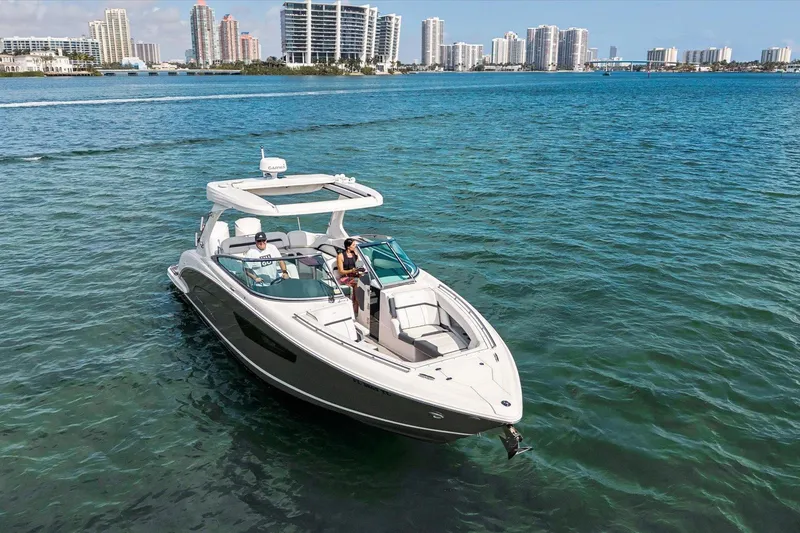 The Image of 2019 Regal 33 OBX boat cruising on clear blue water with city skyline backdrop. - 1