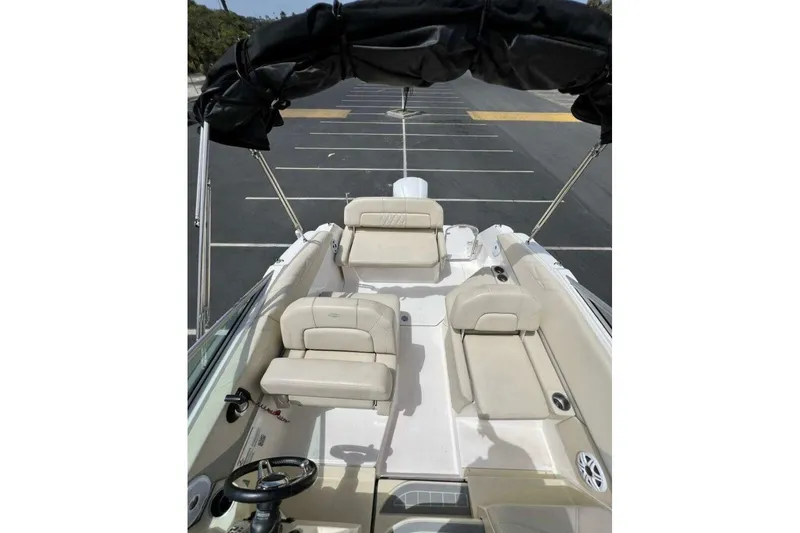 Slide: The Image of 2019 Regal 26 XO boat interior with beige seating and black canopy in a parking lot. - 6