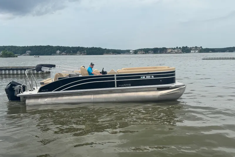 The Image of 2022 Harris Sunliner 250 pontoon boat on a calm lake with scenic background. - 1