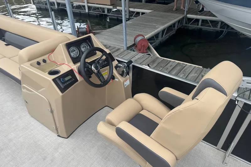 Slide: The Image of 2022 Harris Sunliner 250 boat interior with steering console and captain's chair at dock. - 25