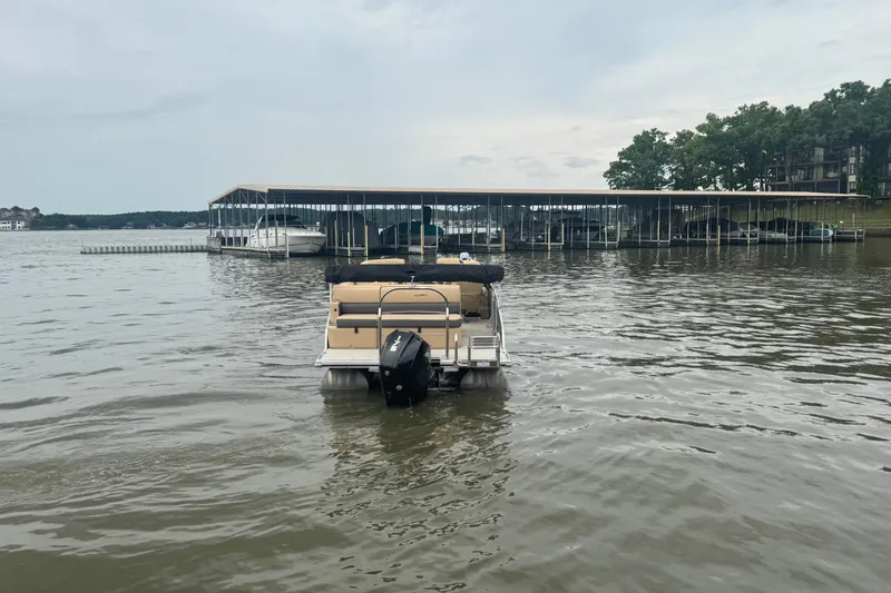 Slide: The Image of 2022 Harris Sunliner 250 pontoon boat on a calm lake near a marina. - 4