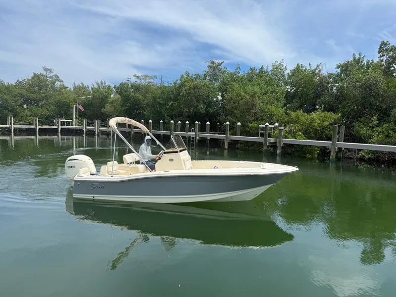 Slide: The Image of Scout 195 Sportfish 2027 on calm water, surrounded by lush greenery. - 0