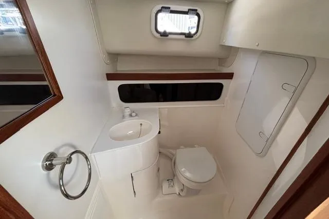 Slide: The Image of 2026 NorthCoast 285 HT boat bathroom with compact sink, toilet, and porthole window. - 9