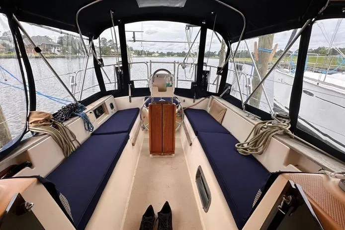 Slide: The Image of 1989 Island Packet 35 sailboat cockpit with blue cushions, docked by a serene waterfront. - 5