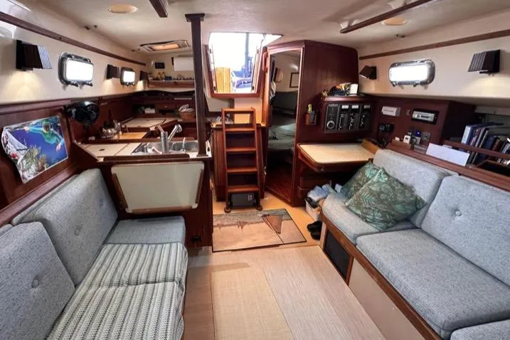 Slide: The Image of Interior of a 1989 Island Packet 35 sailboat, featuring cozy seating and a compact kitchen. - 6