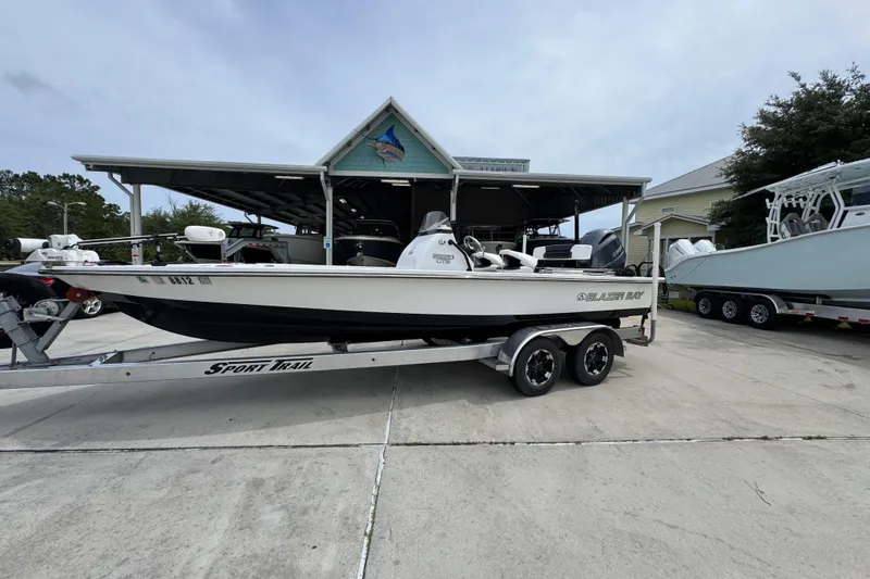 Slide: The Image of 2021 Blazer Bay 2220 GTS boat on a Sport Trail trailer, parked outdoors. - 2