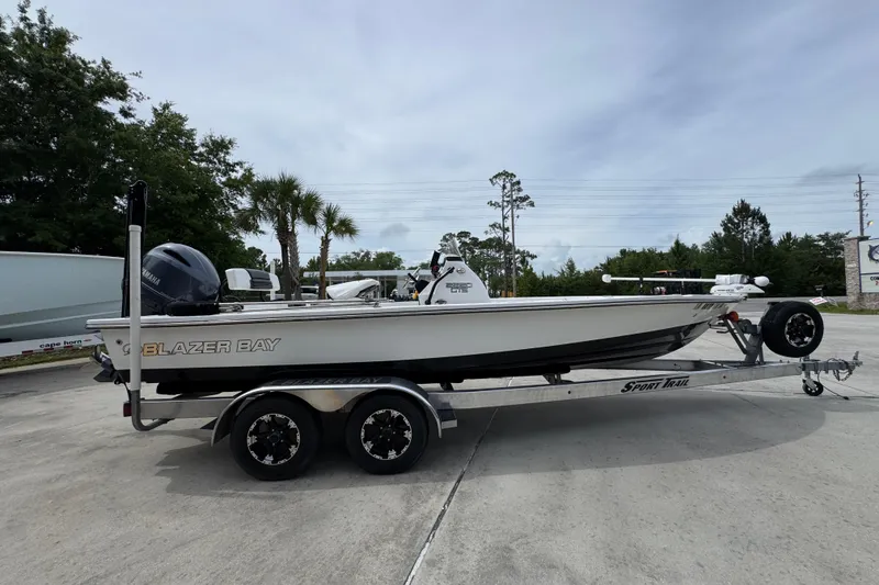 Slide: The Image of 2021 Blazer Bay 2220 GTS boat on trailer, parked outdoors with trees in background. - 8