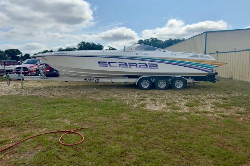 The Image of 1995 Wellcraft Scarab 31 boat on trailer, parked outdoors under cloudy sky. - 0