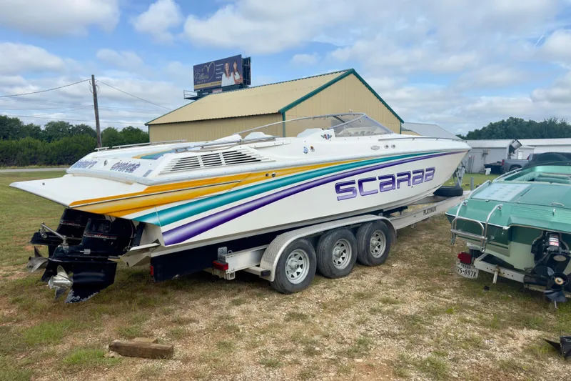 Slide: The Image of 1995 Wellcraft Scarab 31 boat on trailer, vibrant stripes, parked outdoors. - 2