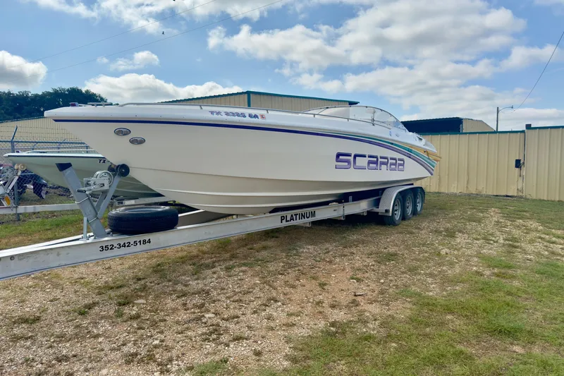 Slide: The Image of 1995 Wellcraft Scarab 31 boat on trailer, parked outdoors under a cloudy sky. - 3
