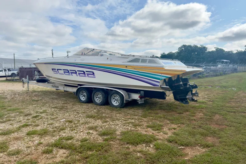 Slide: The Image of 1995 Wellcraft Scarab 31 boat on trailer, featuring vibrant stripes and dual engines. - 4