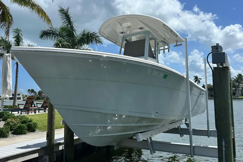 The Image of 2021 Cobia 240 Center Console boat on lift, surrounded by palm trees and waterfront. - 0