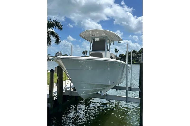 Slide: The Image of 2021 Cobia 240 Center Console boat on lift, sunny day, palm trees in background. - 2