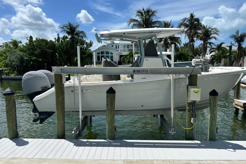 Slide: The Image of 2021 Cobia 240 Center Console boat on lift, docked by palm trees and waterfront home. - 5