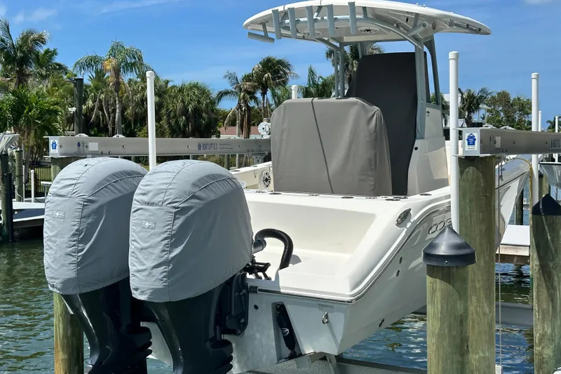 Slide: The Image of 2021 Cobia 240 Center Console boat docked with dual covered engines, surrounded by palm trees. - 6