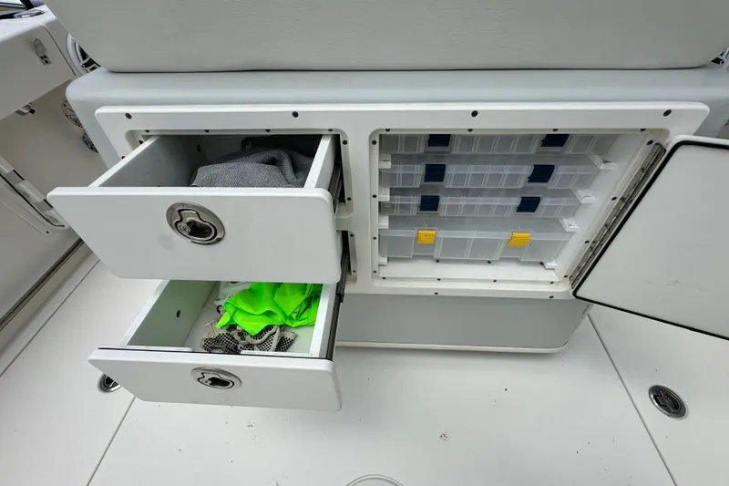 Slide: The Image of Storage compartments on a 2021 Cobia 240 Center Console boat, featuring drawers and tackle boxes. - 83