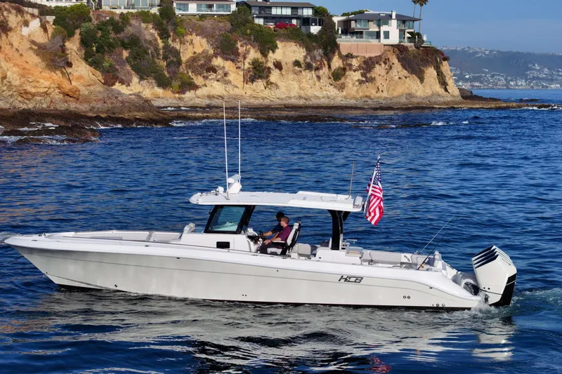 The Image of HCB 42 Lujo 2026 boat cruising near rocky coastline with American flag. - 1