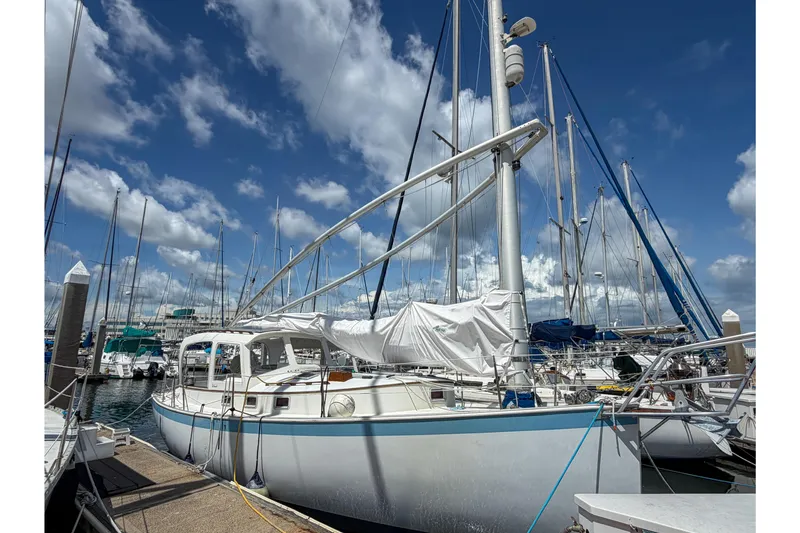 Slide: The Image of 1987 Nonsuch 30 Ultra sailboat docked under a vibrant blue sky with clouds. - 2