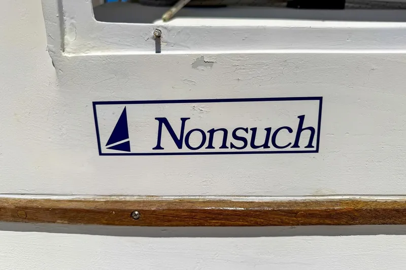 Slide: The Image of Nonsuch 30 Ultra 1987 sailboat logo on white hull with wooden trim. - 30