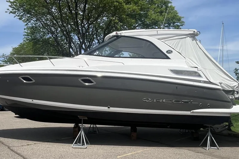 The Image of 2018 Regal 35 Sport Coupe boat on stands, parked outdoors under a clear sky. - 0