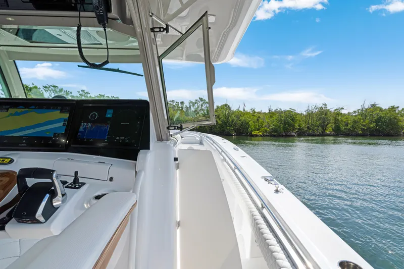 Slide: The Image of Helm of 2027 HCB 53 Suenos boat with navigation screens, cruising near lush shoreline. - 24