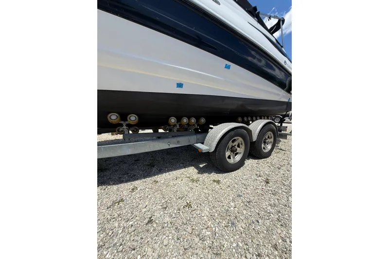 Slide: The Image of 2011 Crownline 236 SC boat on a dual-axle trailer, parked on gravel. - 13