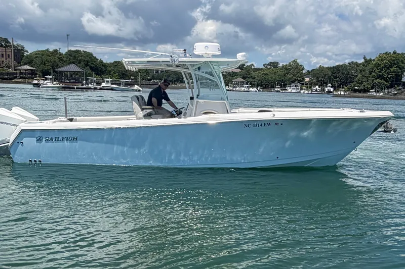 Slide: The Image of 2021 Sailfish 290 CC boat cruising on a sunny day with scenic waterfront background. - 14