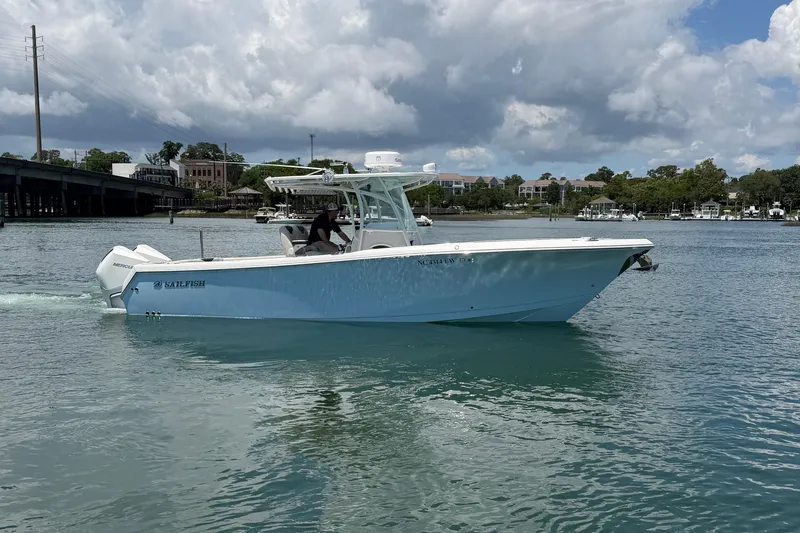 Slide: The Image of 2021 Sailfish 290 CC boat cruising on a calm waterway under a cloudy sky. - 3