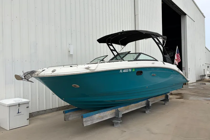 Slide: The Image of 2024 Sea Ray SDX 270 Outboard boat in teal, docked near a large warehouse. - 20