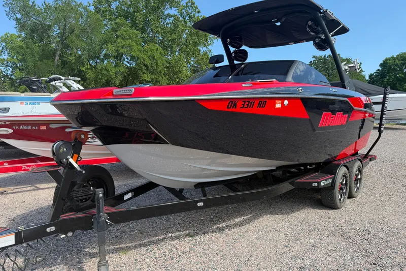 The Image of 2021 Malibu M220 boat in red and black on a trailer, parked outdoors. - 1