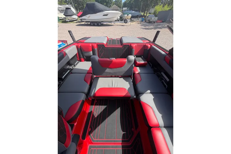 Slide: The Image of Interior of 2021 Malibu M220 boat with red and gray seating, parked outdoors. - 15