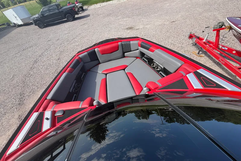 Slide: The Image of 2021 Malibu M220 boat with red and gray seating, parked on gravel. - 19